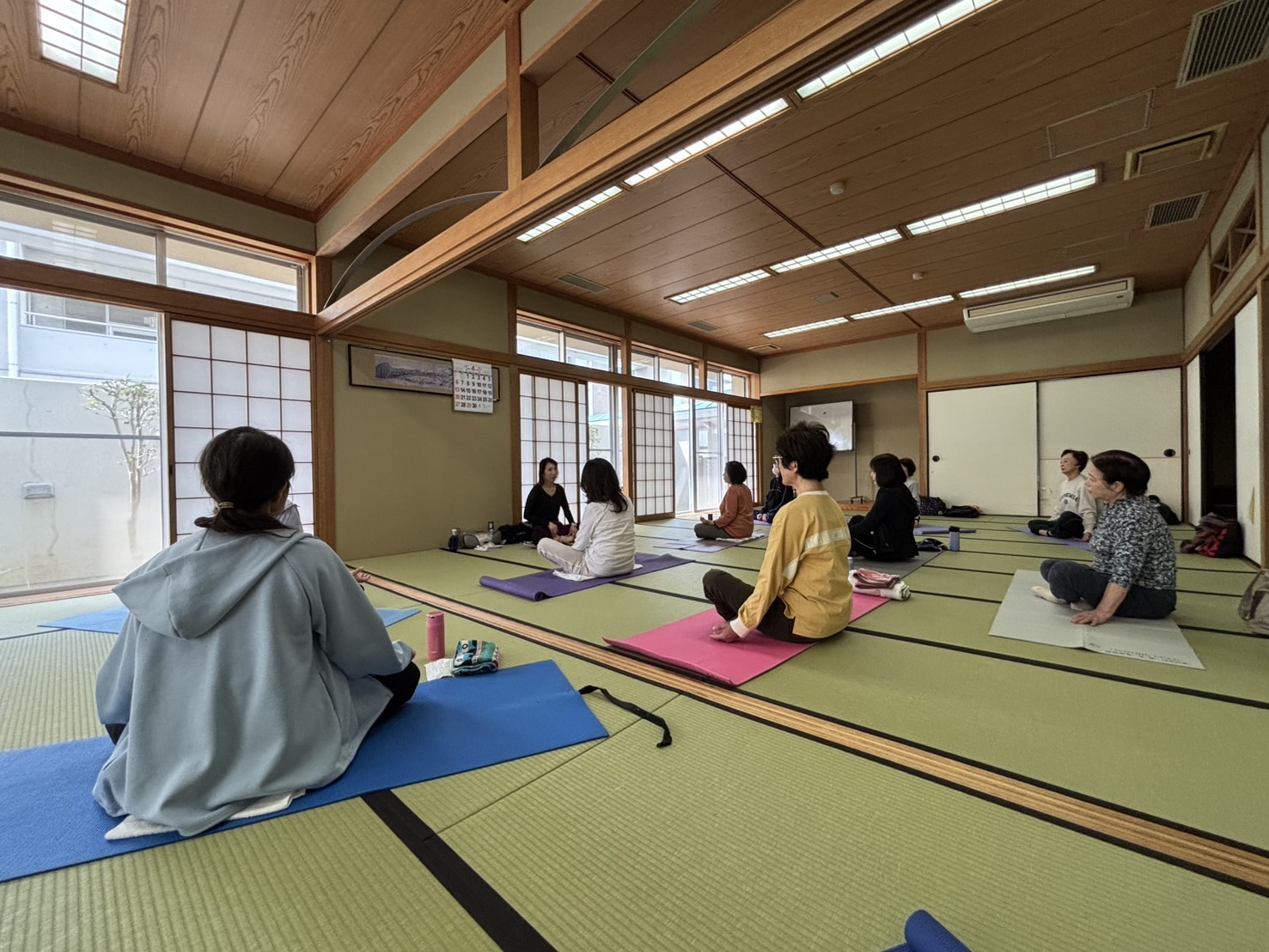 ピラティス教室の様子。和室にヨガマットをひいて、教室生徒がピラティスに励んでいます。奥に講師の先生がいます。