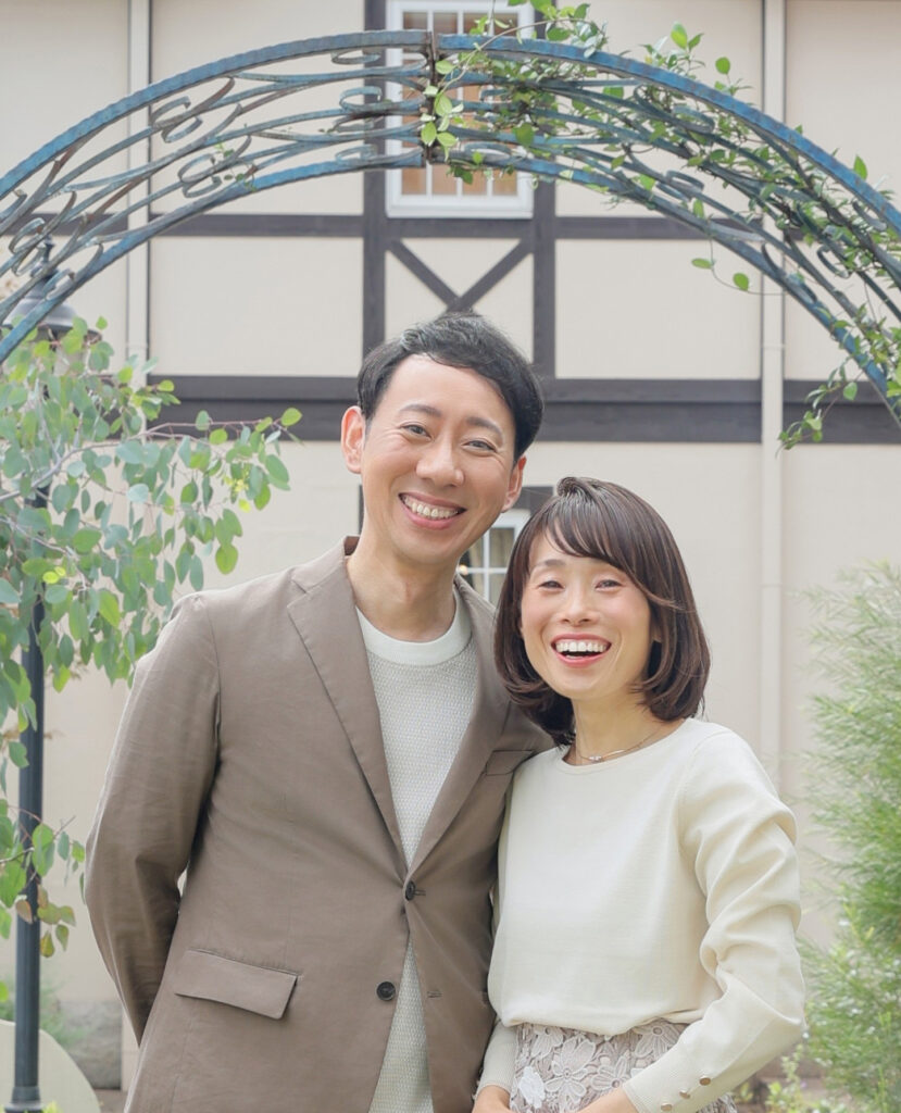田形夫婦の写真です。夫婦である男女がアーチ形のオブジェの前に立ち笑顔でこちらを見ています。