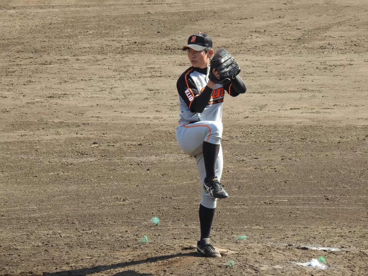 BAN BASEBALL CLUBの試合風景。土のグラウンドで、ユニフォームに「GIANTS」と記された投手が片足を高く上げ、力強くボールを投げようとする瞬間を捉えた一枚。集中した表情と躍動感あるフォームが、競技への真剣な姿勢とチームの熱意を伝えている。