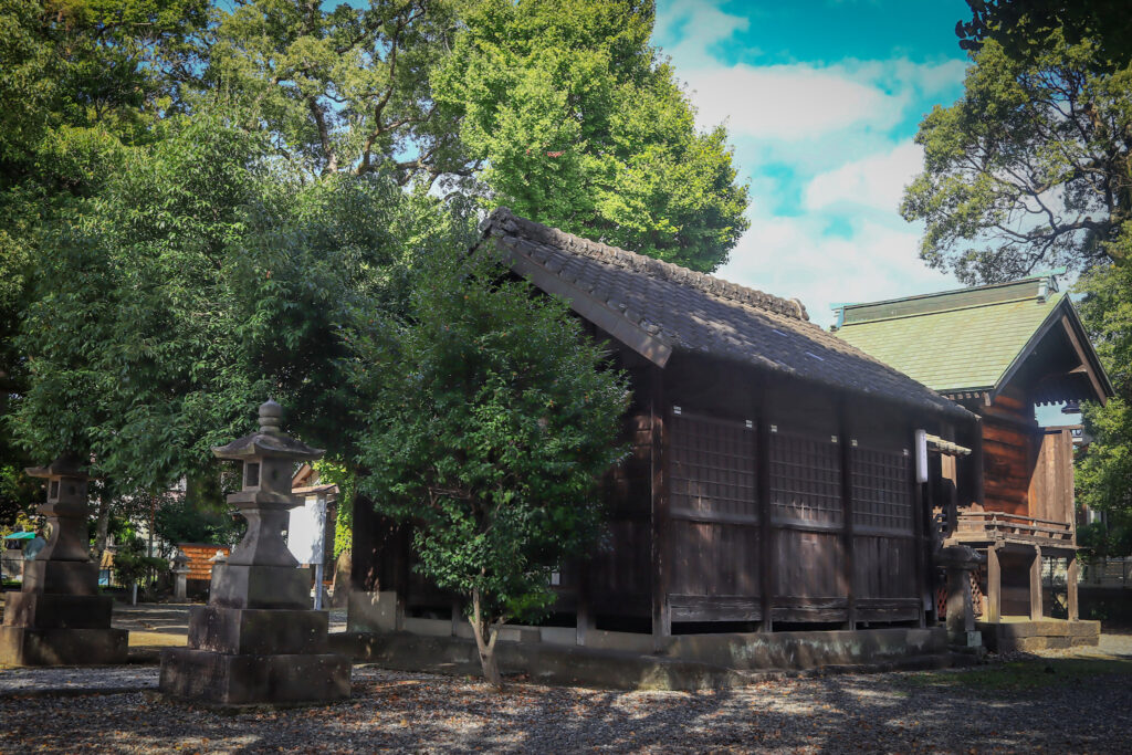 大分市古国府に佇む「大国社」の境内風景。木造の社殿は瓦屋根と格子の意匠が美しく、周囲には緑豊かな木々が広がる。前景には石灯籠が並び、柔らかな陽光が差し込む静謐な空間が広がる。自然と調和した神聖な佇まいが、地域の歴史と信仰の深さを感じさせる。