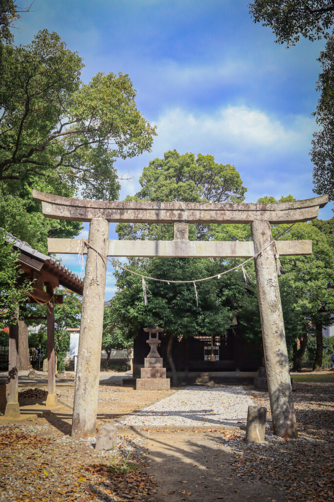 大分市古国府の「大国社」参道入口に立つ石造りの鳥居。しめ縄と紙垂が掛けられ、神聖な空間への境界を示している。鳥居の奥には石灯籠と木々に囲まれた参道が続き、青空の下で静けさと厳かさが漂う。自然と信仰が調和する、地域に根差した神社の風景。