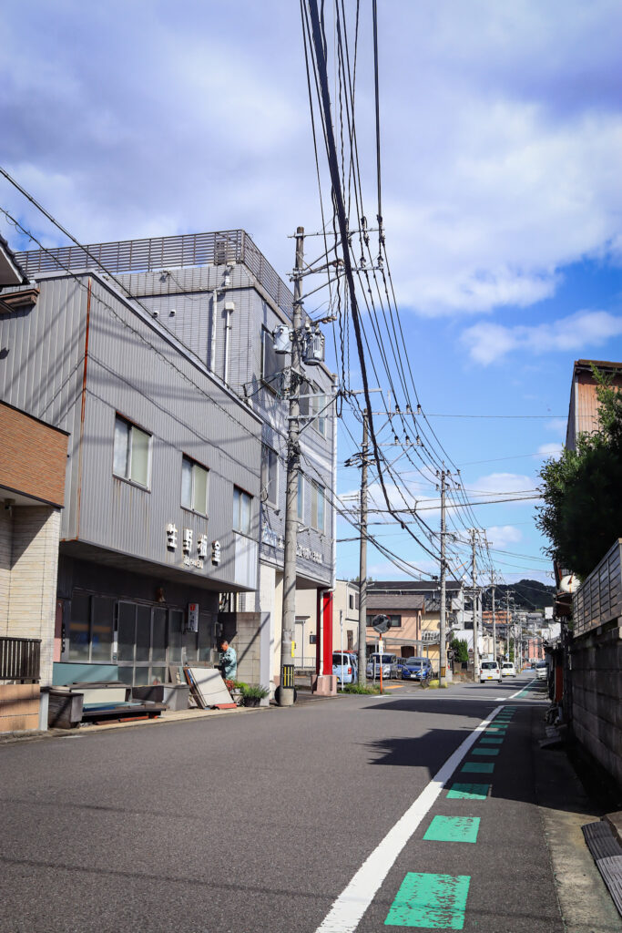 南大分・三ケ田町の目抜き通り。板金屋さんの看板が見える建物と穏やかな街並み