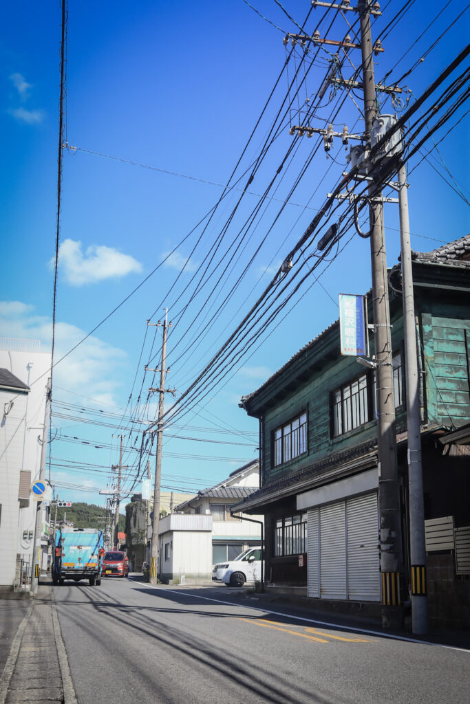 南大分・三ケ田町の目抜き通り。晴天の下、緑の建物や電線が印象的な街並み