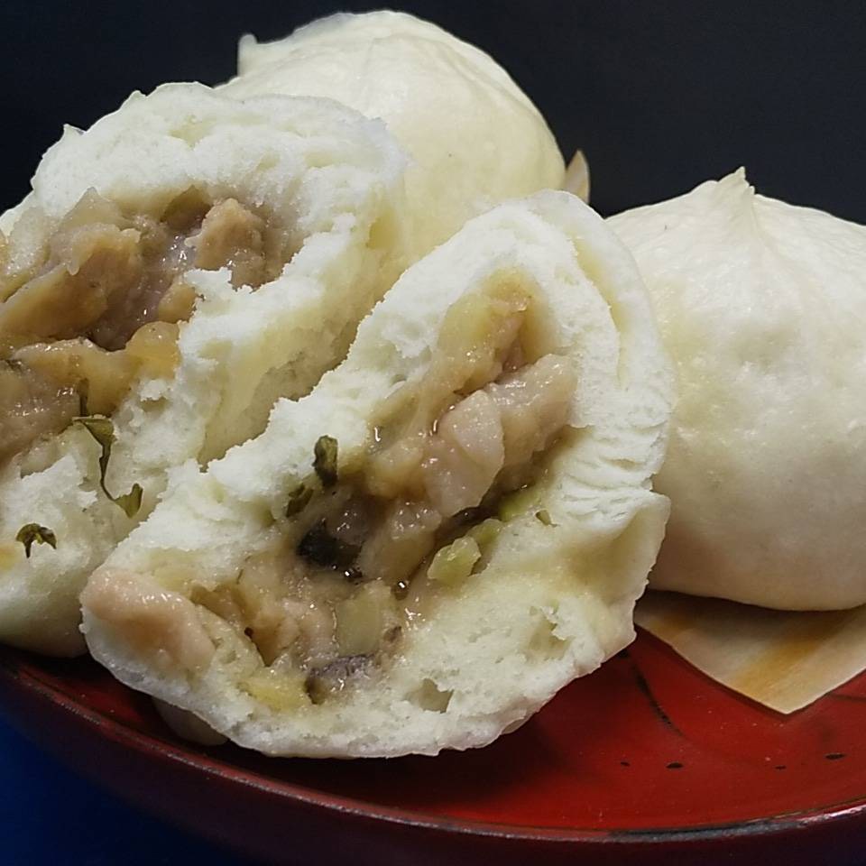 中華一楽にくまんやの肉まんの写真。ふっくらとした白い皮の肉まんが皿に並び、ひとつは半分に割られて中の具材が見えている。肉と野菜が詰まった温かい餡がつややかに輝き、湯気が立ちのぼるような、できたての美味しさを感じさせる一枚。